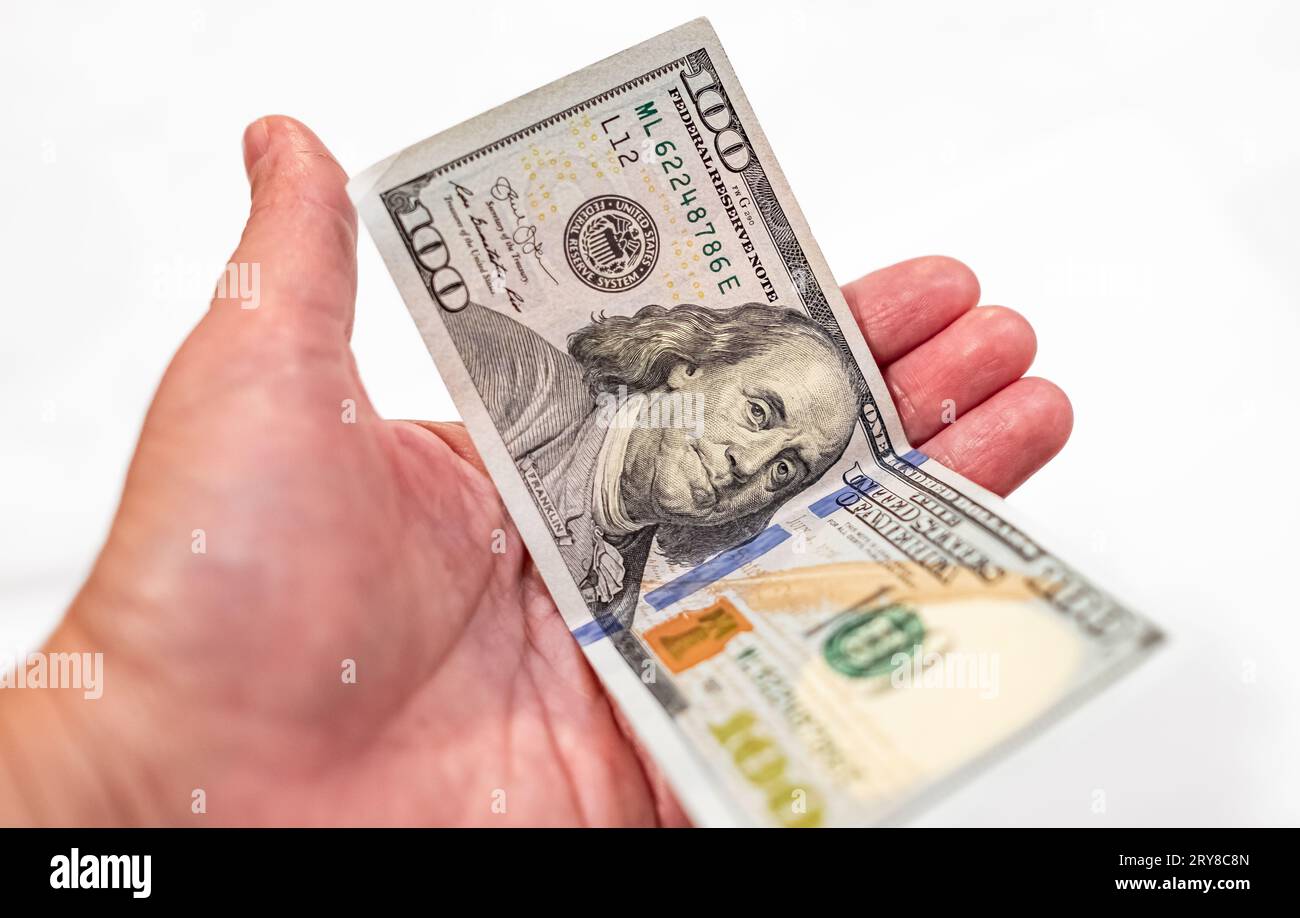 Hand holding one dollar isolated on white background. Man or woman hand giving 100 dollar bill. One hundred us dollars in a hand. Currency exchange, f Stock Photo