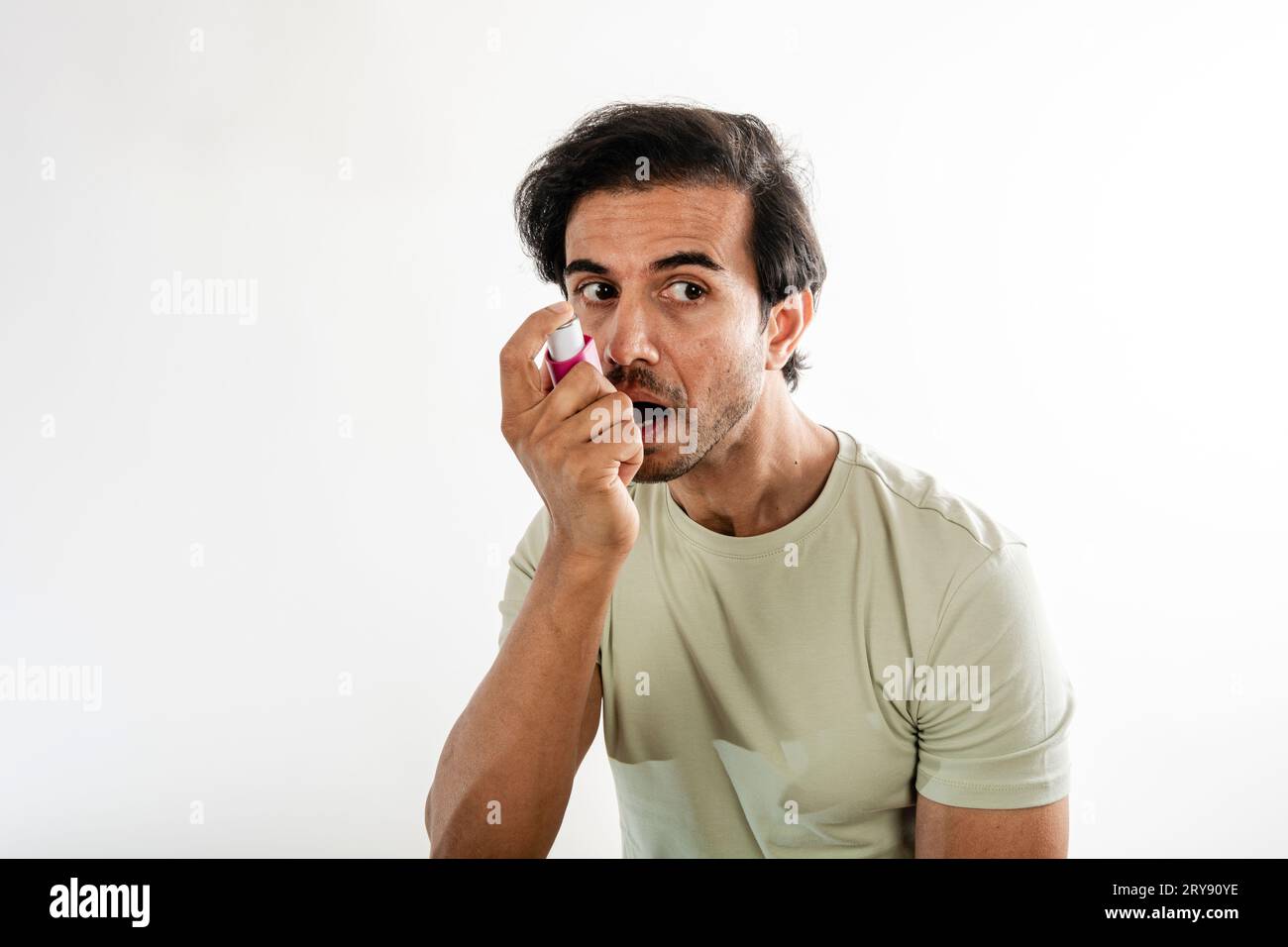 Asian young man from india using a respiratory inhaler. Study shot on white background, selective focus. Stock Photo