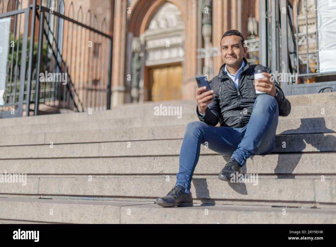 Young latino man sitting on some stairs of a church. Stock Photo