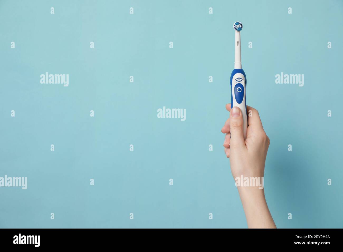 Woman holding electric toothbrush on light blue background, closeup ...