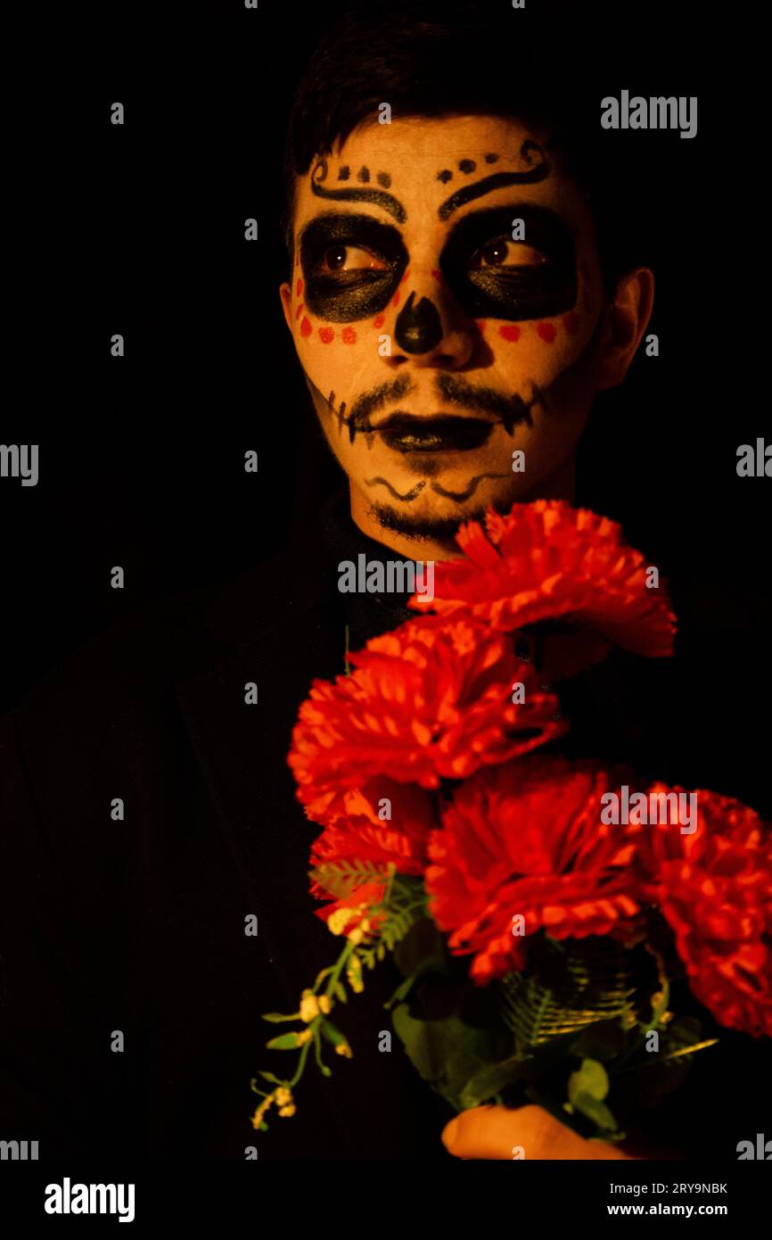 young man dressed as catrin character holding a bouquet of red flowers