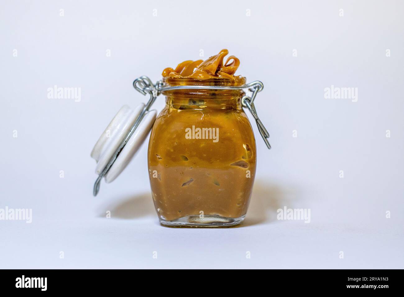 Uncovered jar of dulce de leche overflowing. Stock Photo