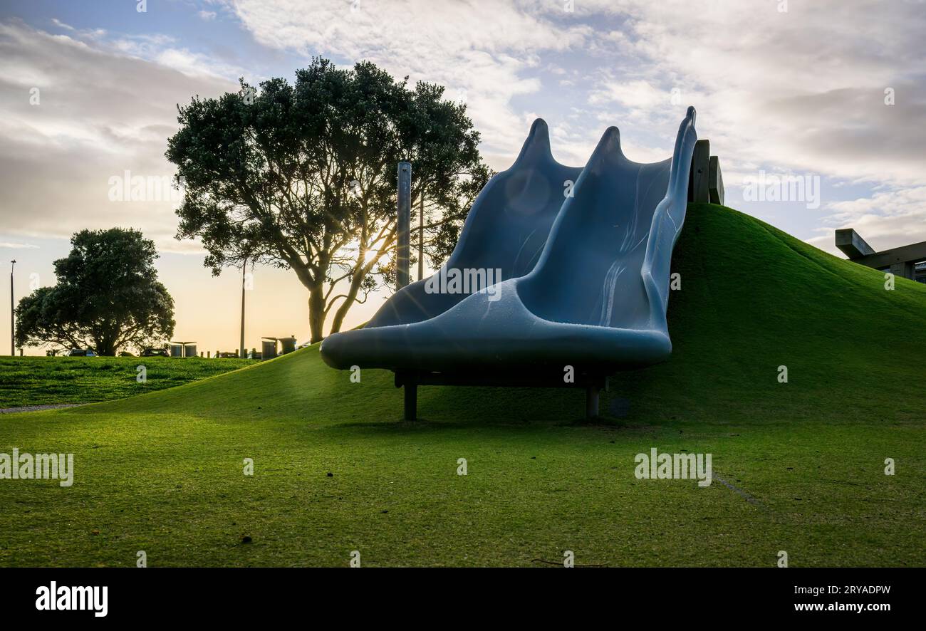 Empty playground slide and Pohutukawa tree at sunrise. Auckland. Stock Photo