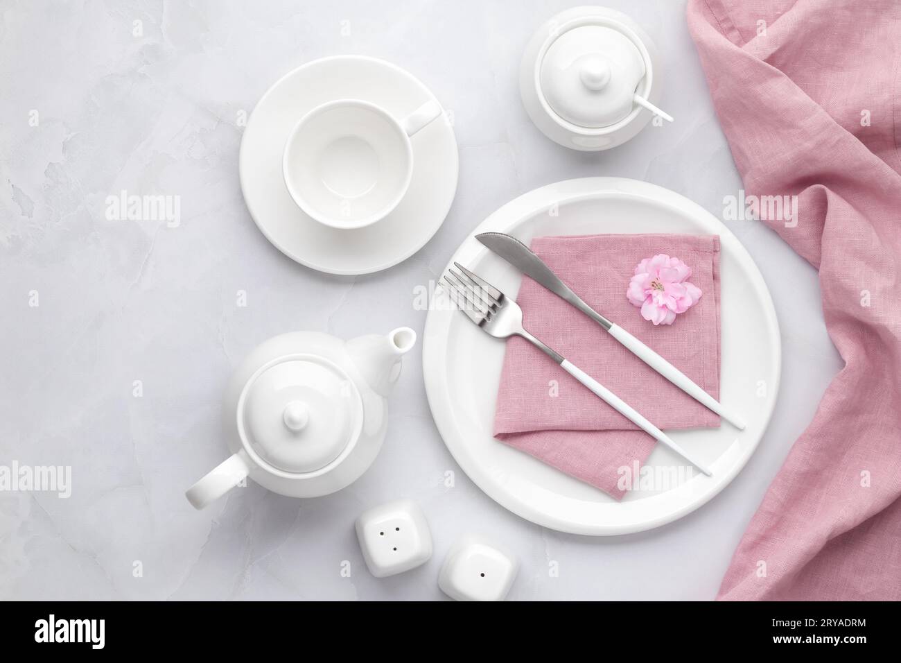 White ceramic tableware and cutlery. Utensil dishware, crockery, teapot and cup on grey marble background, table setting with empty plate, fork and kn Stock Photo