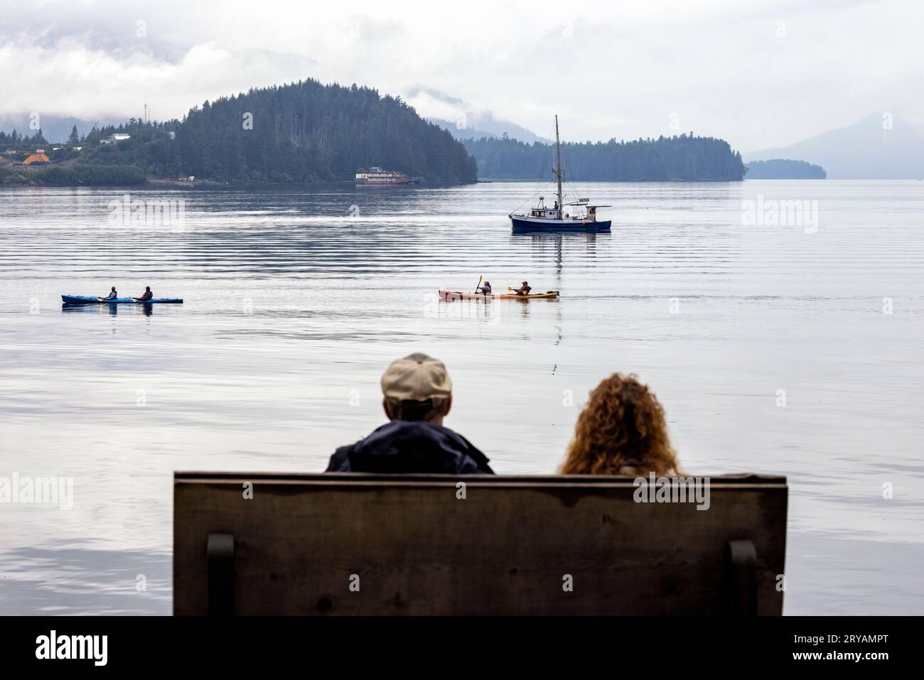 Couple sitting on bench watching kayakers in Hoonah, Alaska, USA Stock Photo