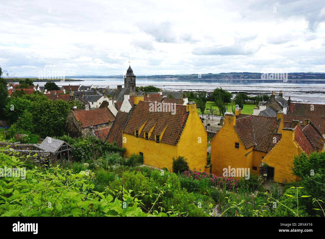 Historic buildings in the Village of Culross, Scotland, with bright yellow ochre paint and terra cotta clay roof tiles. The Firth of Forth lies beyond Stock Photo