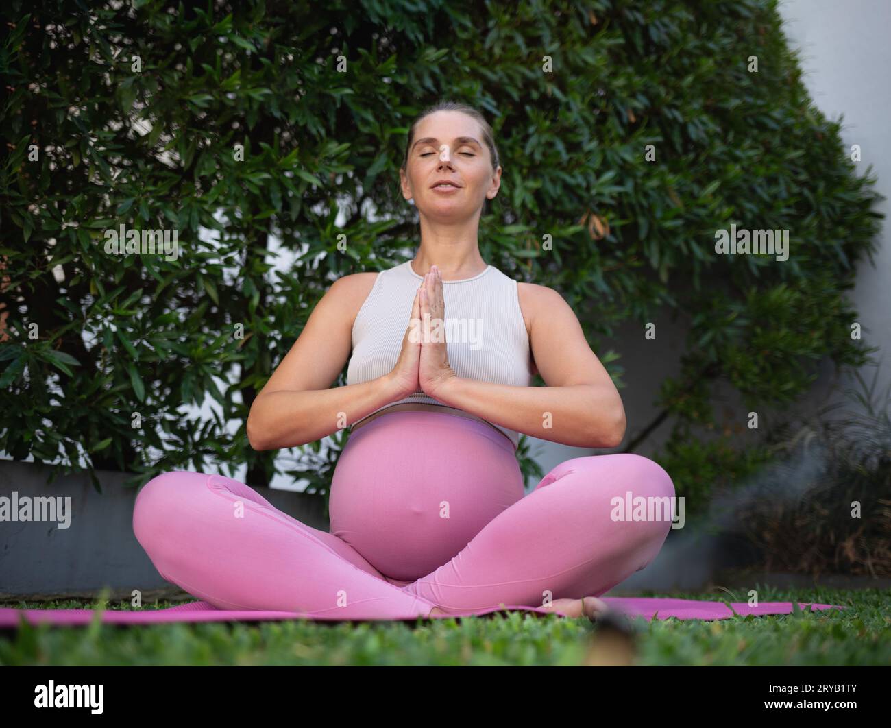 young beautiful pregnant woman meditates sitting on a yoga mat on a green lawn. relaxation and healthy lifestyle concept Stock Photo