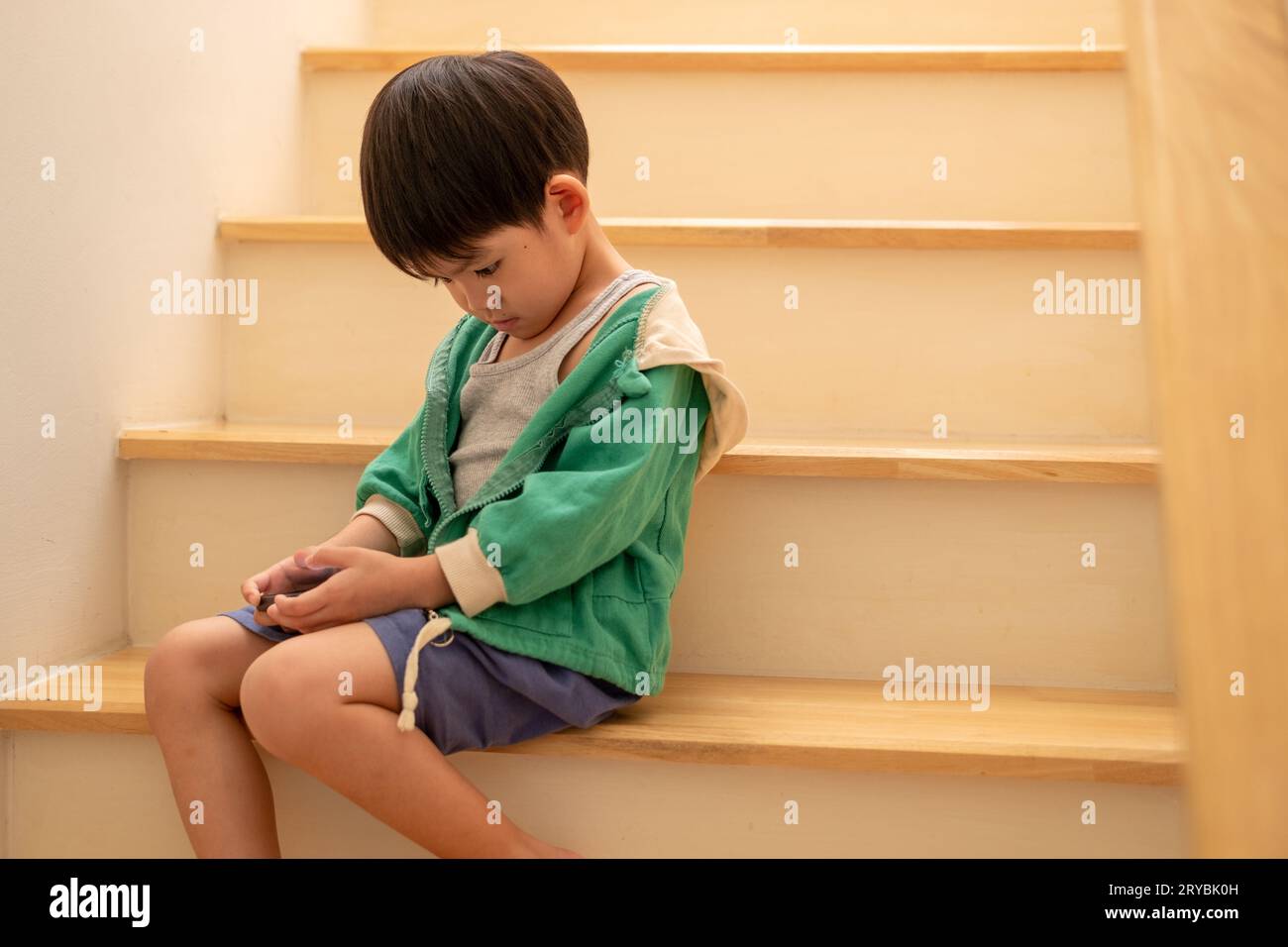 A boy who was scolded by his mother secretly came to play on the phone on the stairs. Stock Photo