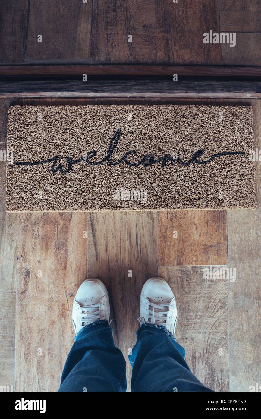 High angle view of welcome mat in door over wooden floor with woman foot-ware near of it Stock Photo