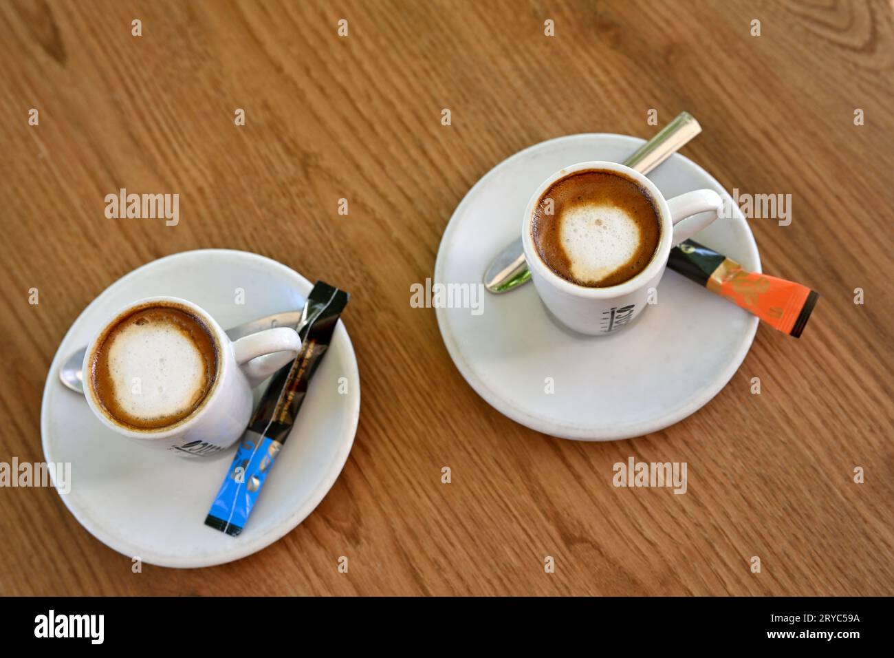 Two cups of coffee with packs of sugar on saucer, wooden table top Stock Photo