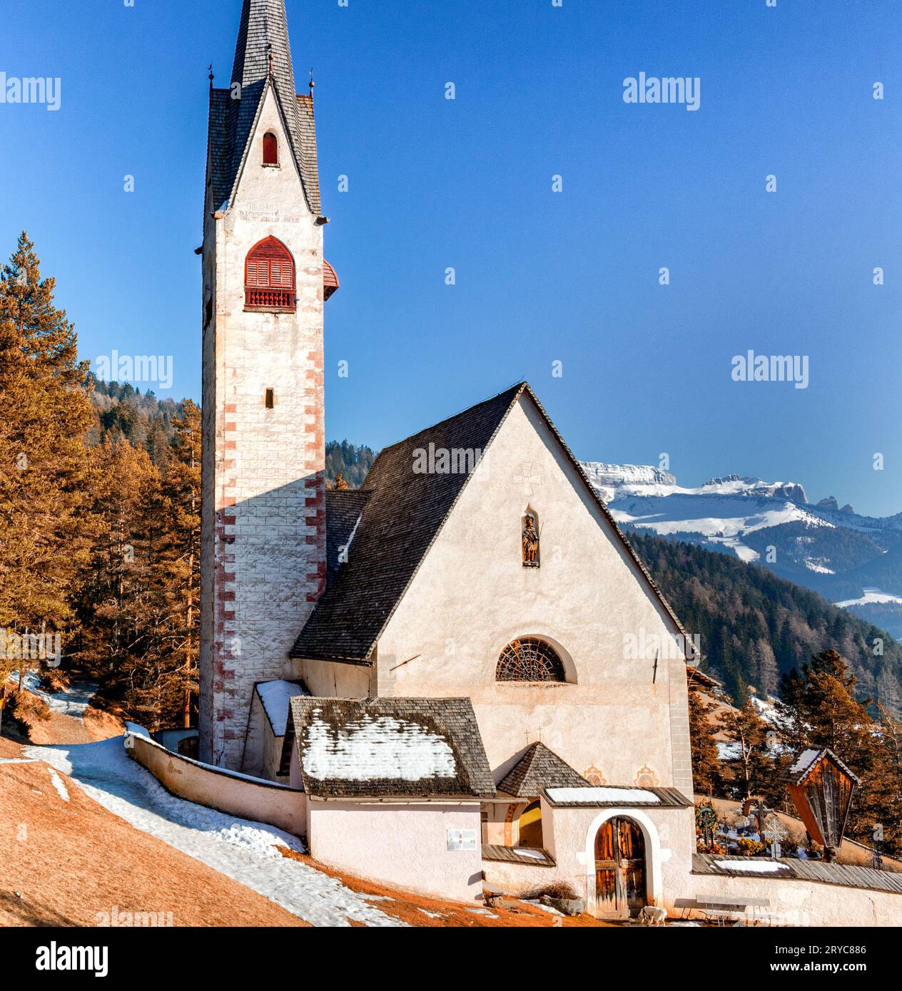 Church of St. Jacob overlooking pine forests and snow-capped peaks in winter Stock Photo