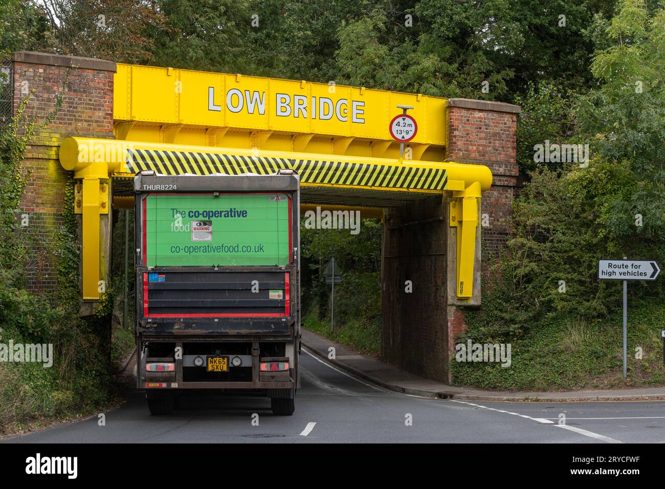 A railway bridge frequently hit by high vehicles lorries trucks recently painted bright yellow, Wrecclesham, Surrey, England, UK. Low bridge Stock Photo