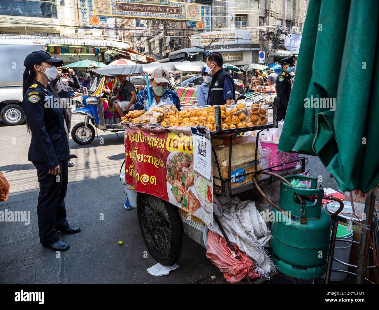 Hectic Bangkok street: A vibrant food vendor and a lady in blue against the iconic tuk-tuk backdrop, embodying the city's energy and charm. Stock Photo
