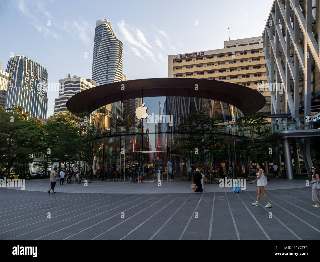 An Apple store in Bangkok, Thailand, featuring reflections on its glass facade as people stroll nearby. Stock Photo