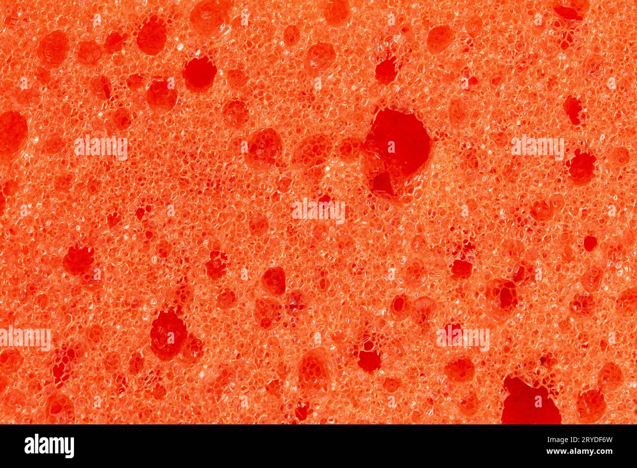 Abstract embossed orange background - the surface of a soft sanitary sponge. Orange foam sponge close-up Stock Photo