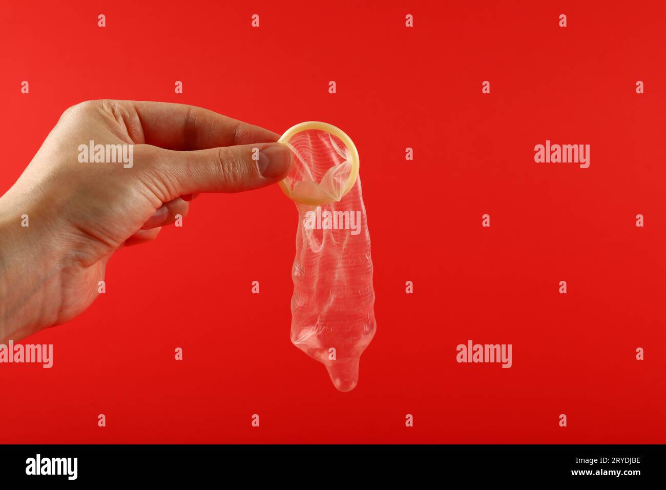 Close up man hand holding open condom over red Stock Photo