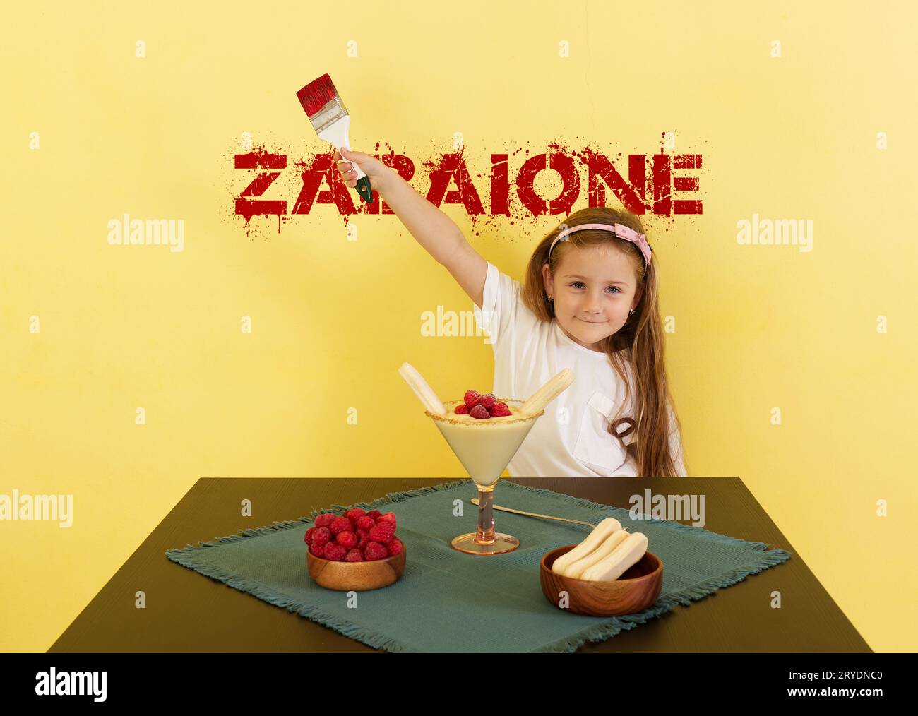 Cute little baby girl celebrating at home and posing funny at the table with traditional Italian dessert zabaione. Stock Photo