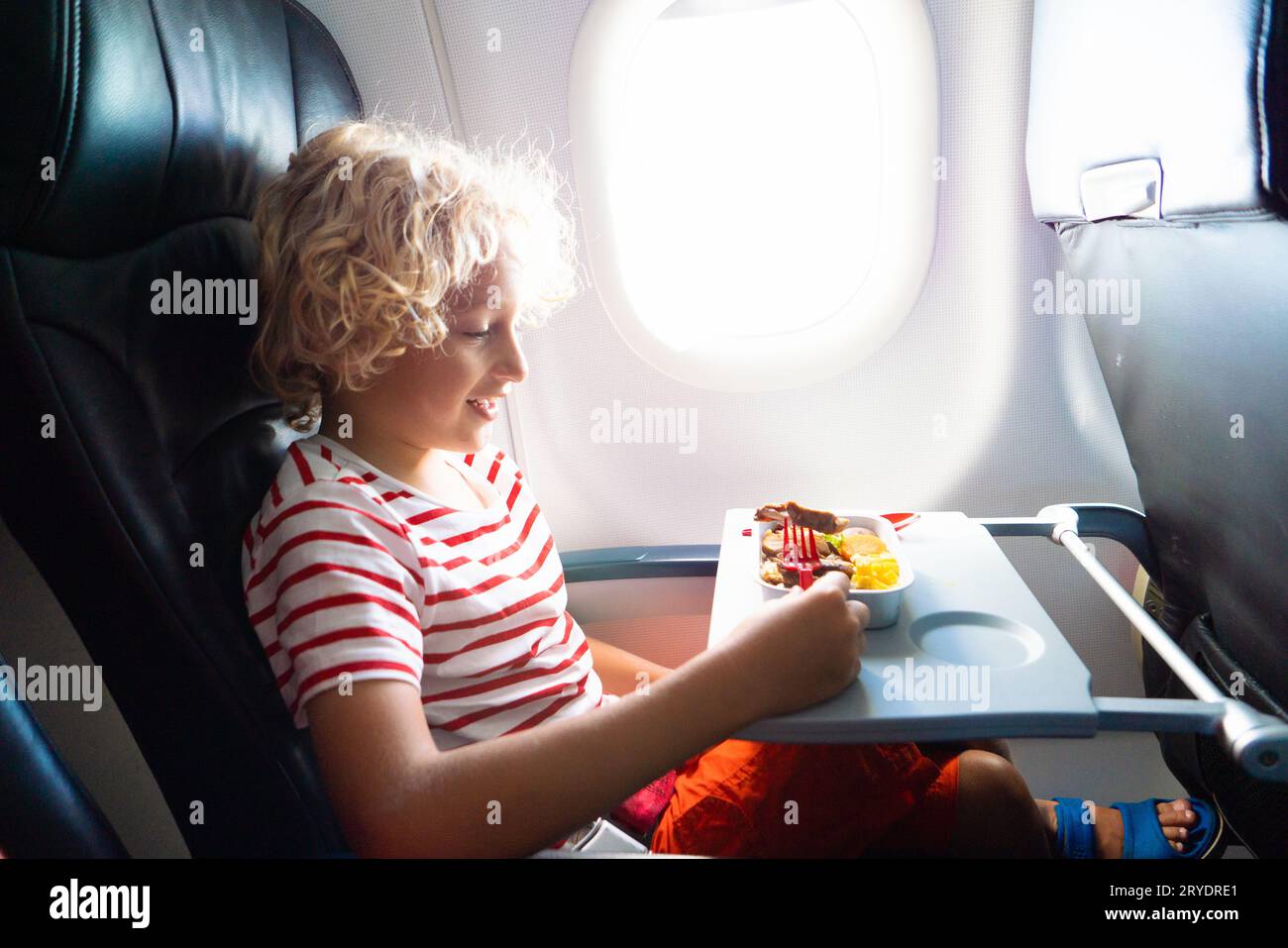 Child in airplane window seat. Kids flight meal. Children fly. Special inflight menu, food and drink for baby and kid. Boy eating healthy lunch Stock Photo