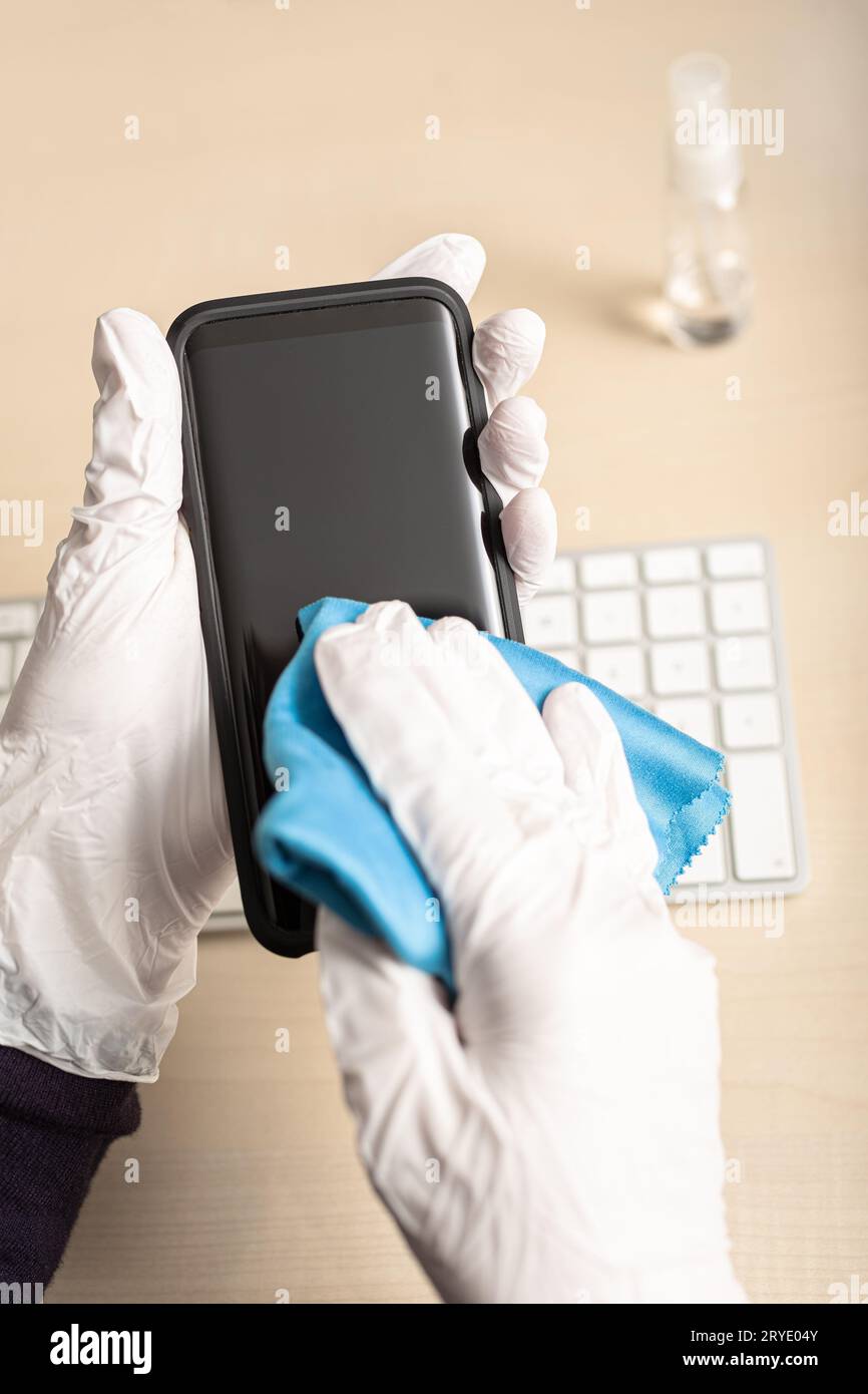 Hands with glove cleaning mobile phone with disinfectant Stock Photo
