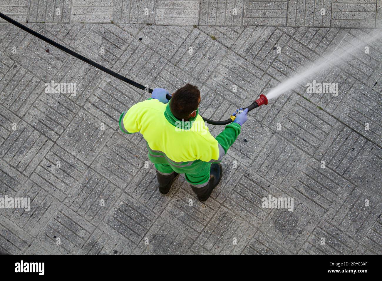 Worker holding a hose cleaning the sidewalk with water Stock Photo