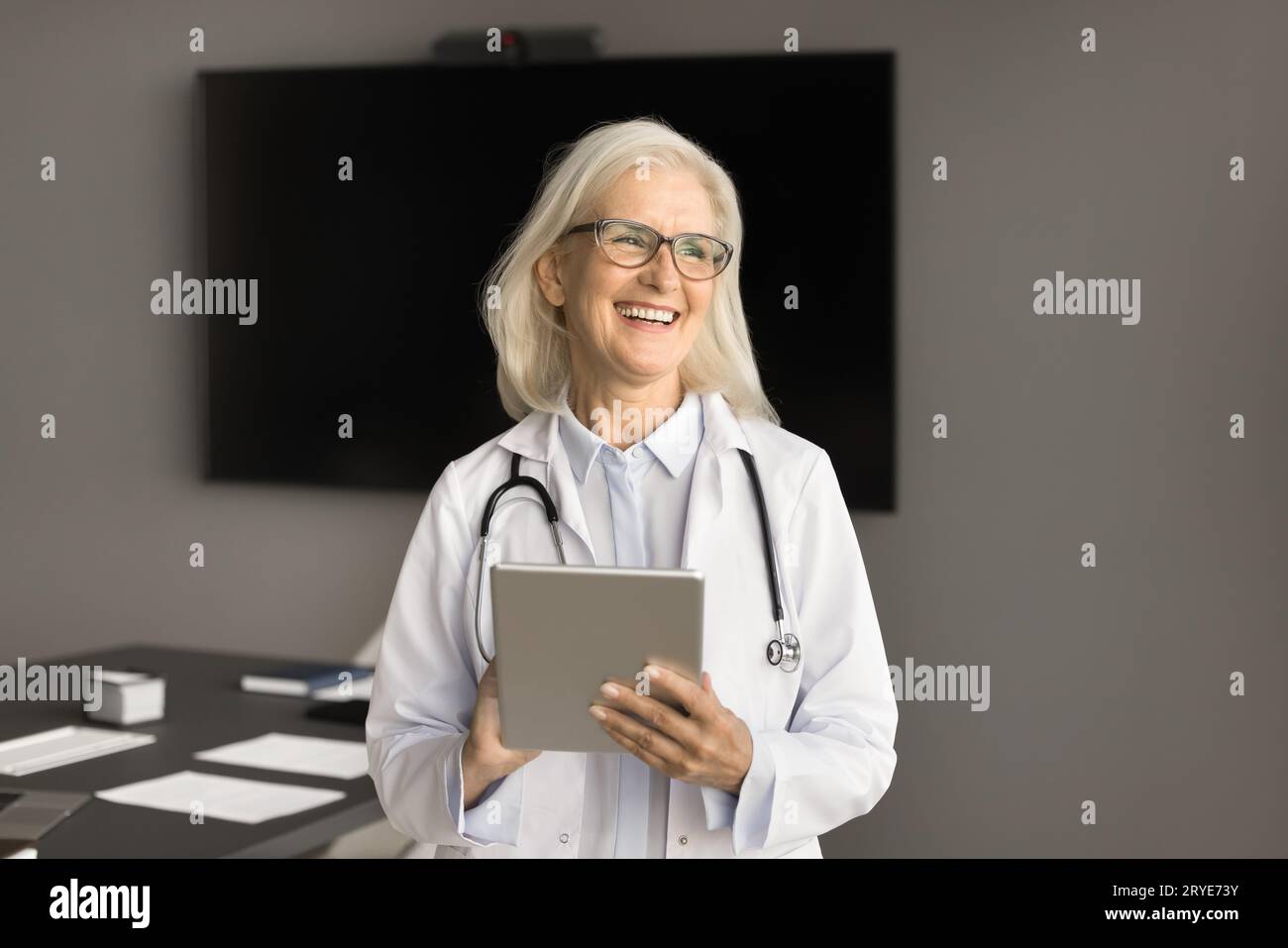 Positive older chief doctor in white coat using tablet computer Stock Photo