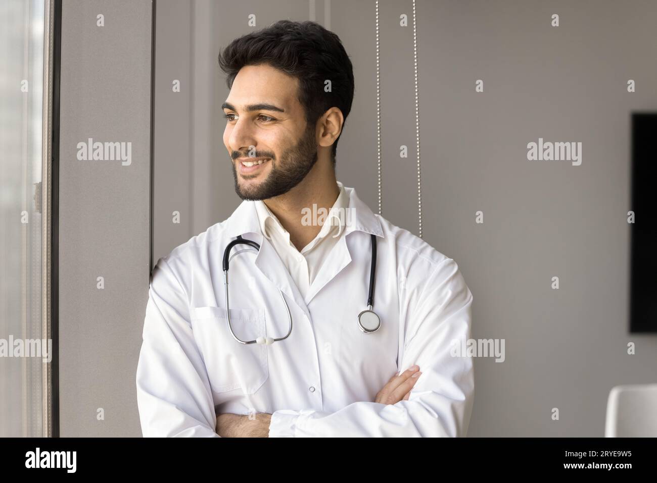 Positive successful Arab doctor man standing at window Stock Photo