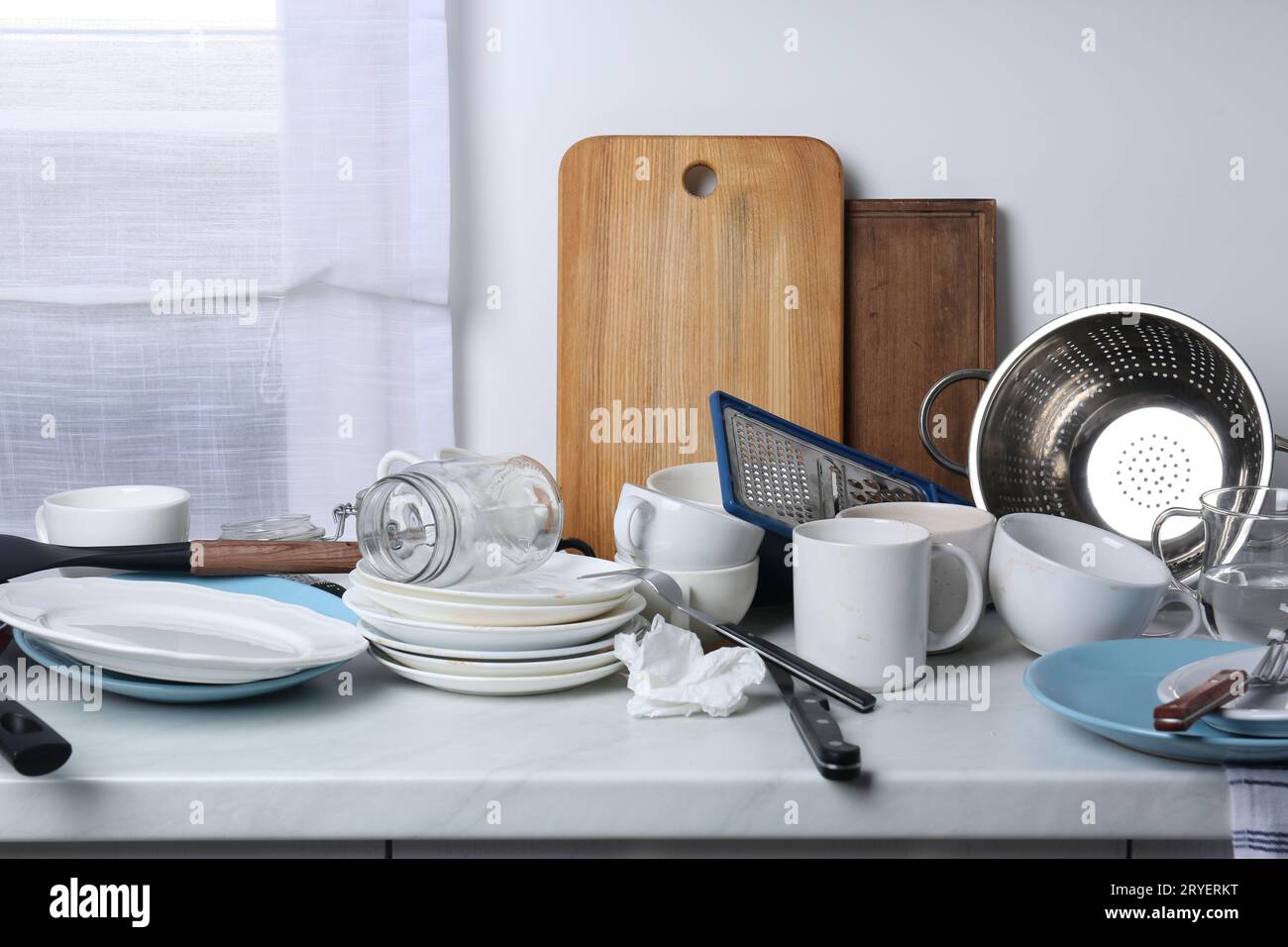 Many dirty utensils and dishware on countertop in messy kitchen Stock Photo