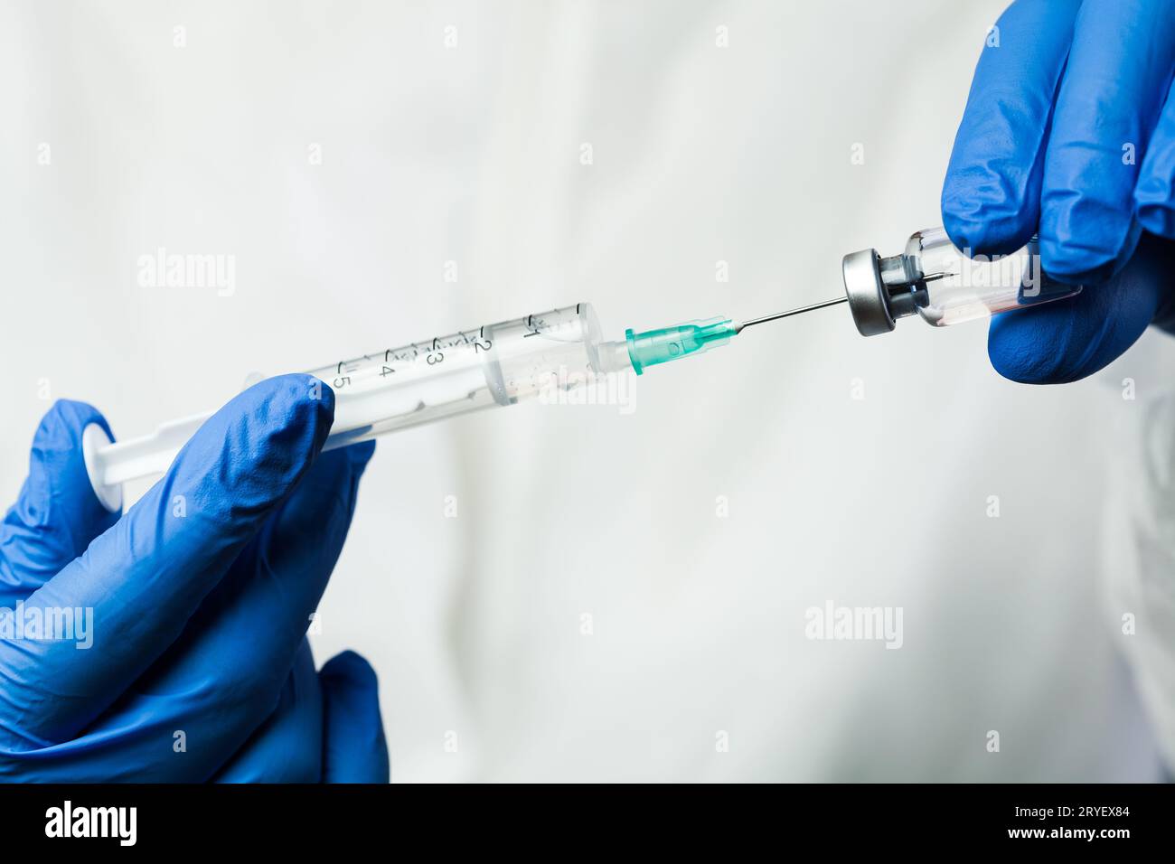 Nurse of NHS medical lab technician inserting syringe needle into glass vial bottle Stock Photo