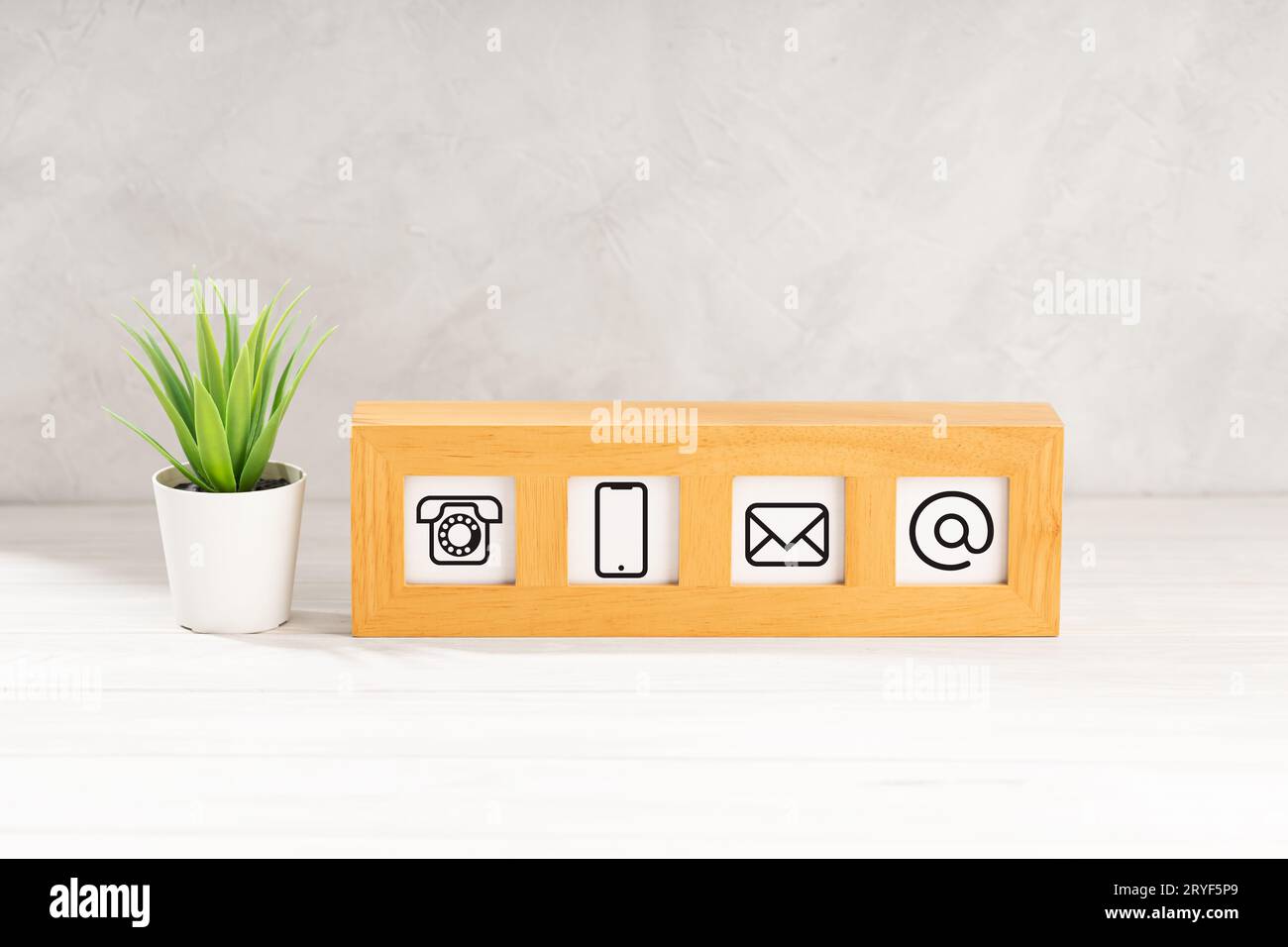 Contact us icons in modern wooden frame on desk. White textured wall. Copy space Stock Photo