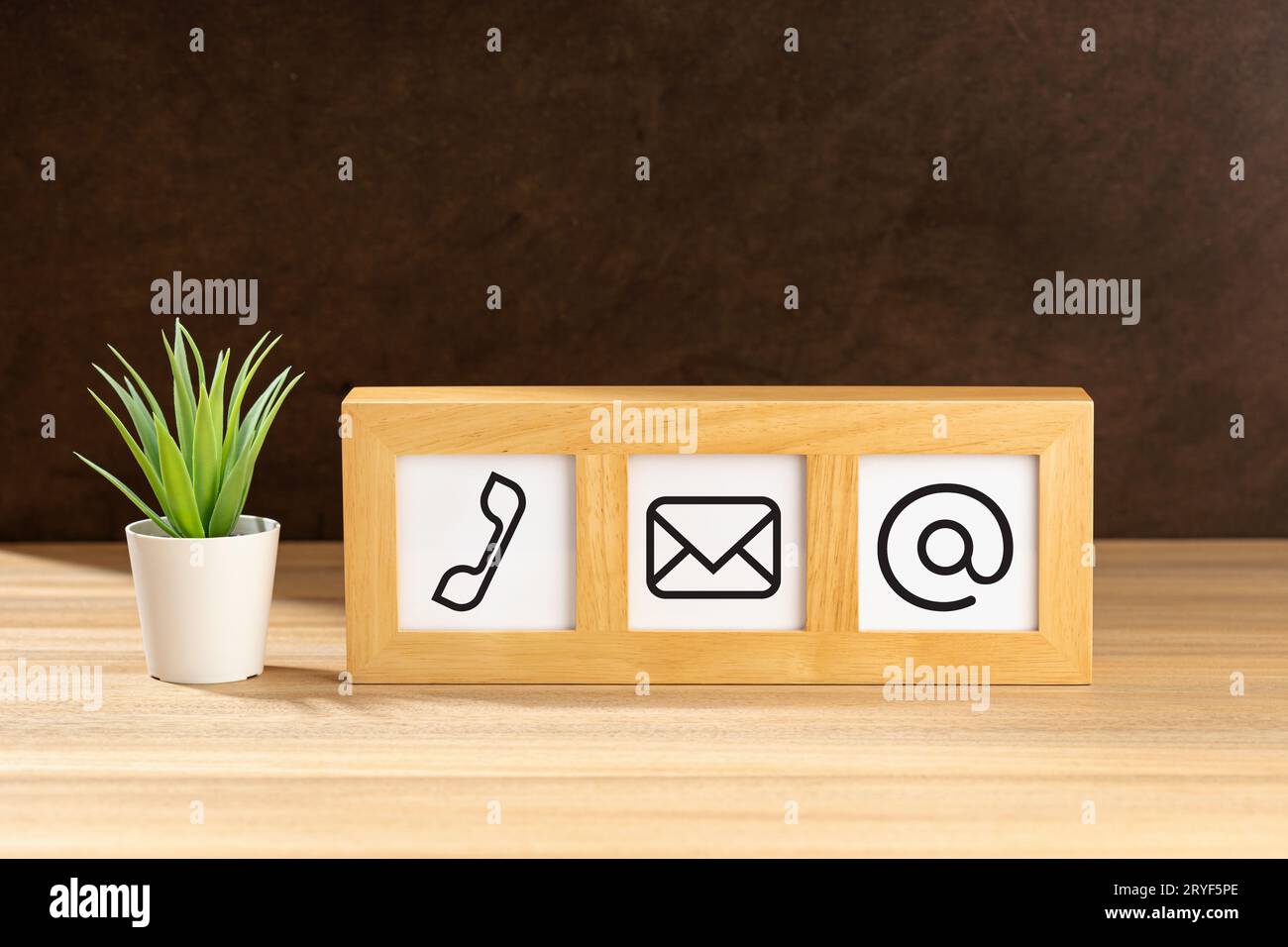 Contact us icons in modern wooden frame on desk. Brown textured wall. Copy space Stock Photo