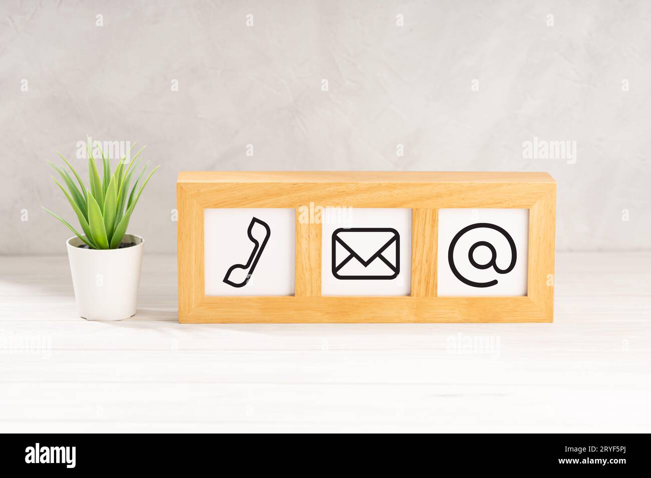 Contact us icons in modern wooden frame on desk. White textured wall. Copy space Stock Photo