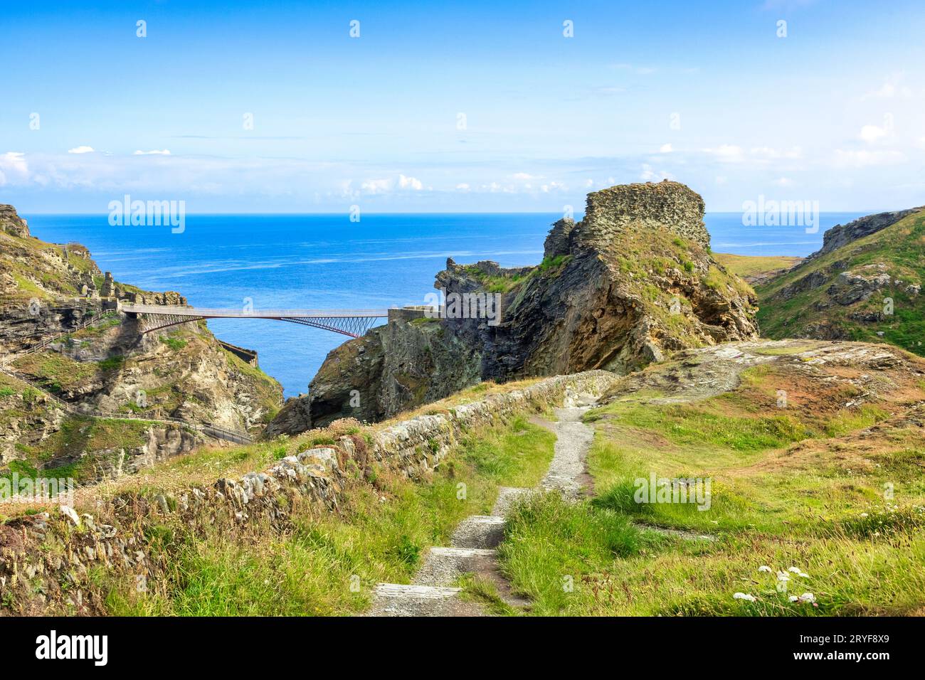 21 June 2023: Tintagel Castle, Cornwall, UK - and its famous double cantilever bridge, from the South West Coast Path. The castle is the legendary... Stock Photo