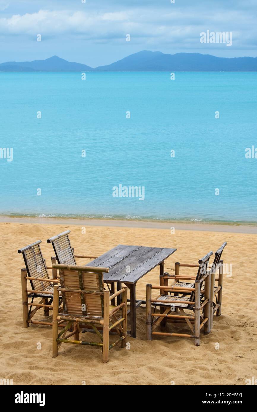 Wooden bamboo furniture, table and five chairs around on sand beach