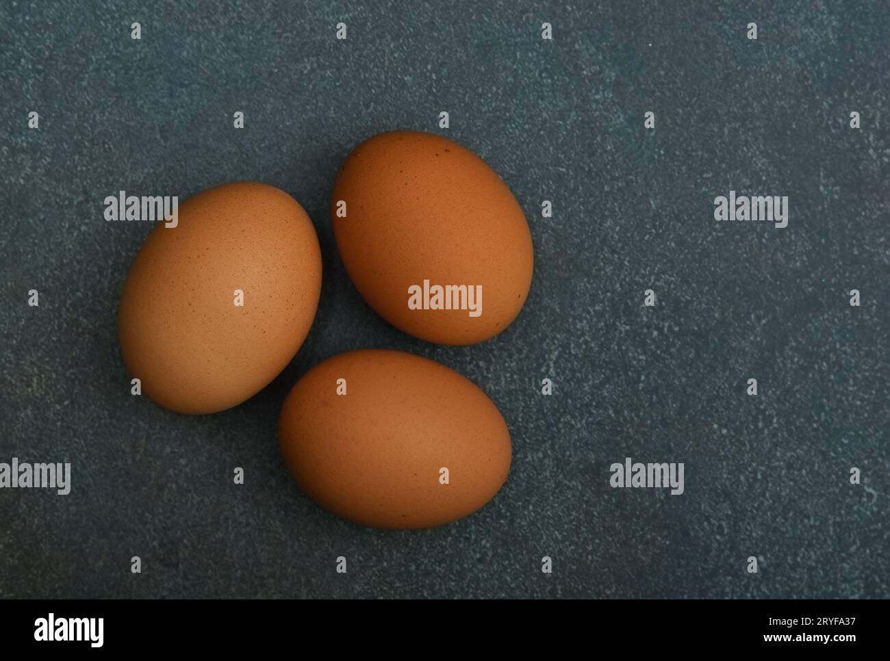 Three brown chicken eggs on dark table Stock Photo
