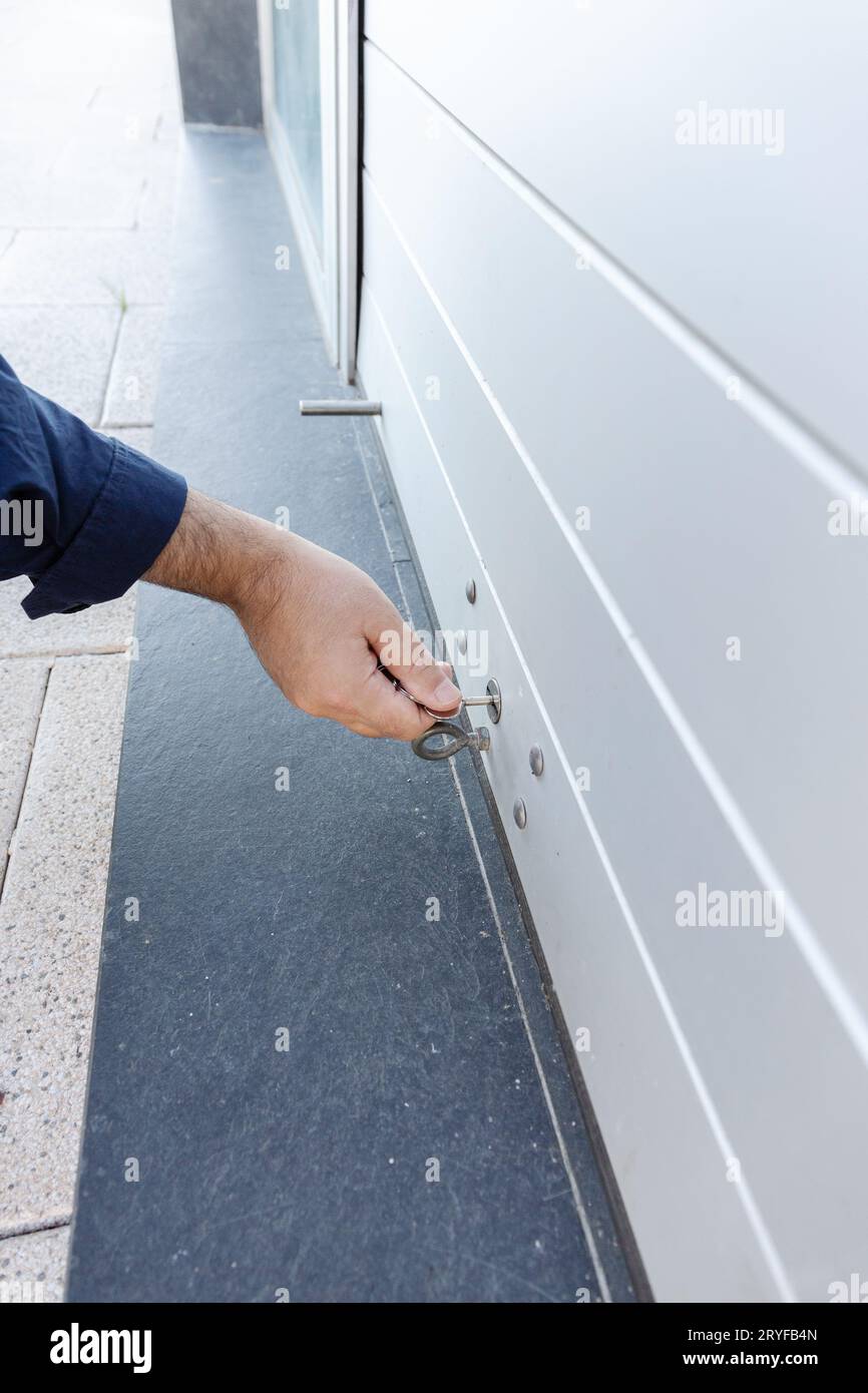 Hand with a key closing a roller shutter door of a store. Closing