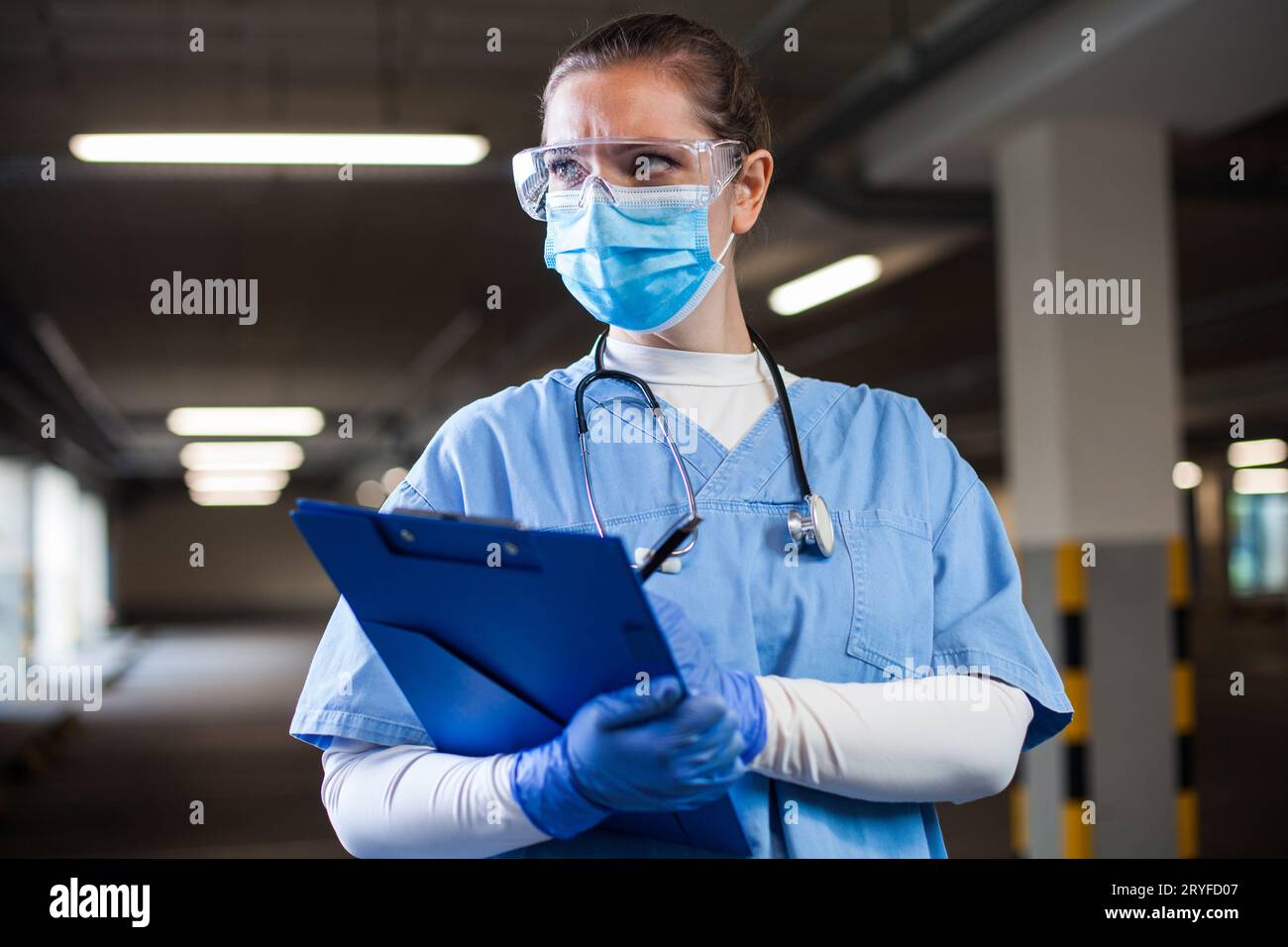 Young serious UK NHS doctor wearing blue scrubs,protective goggles and