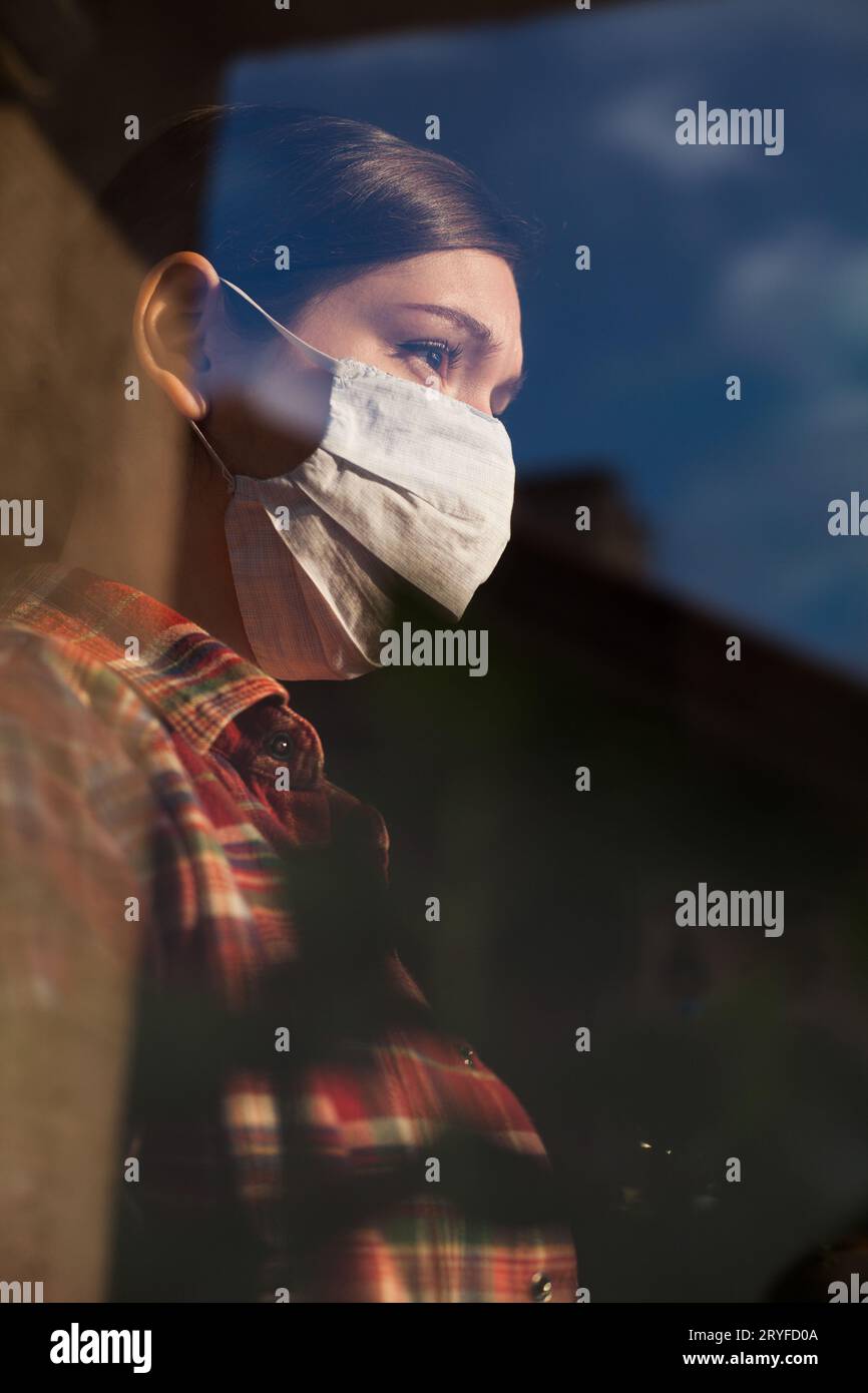 Young woman wearing face mask looking through the window Stock Photo