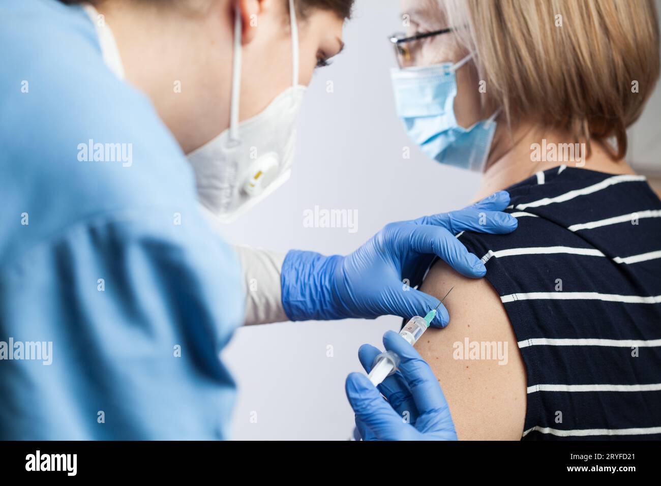 Female medical worker injecting Coronavirus booster dose to elderly patient Stock Photo