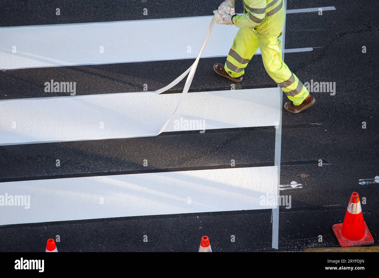 Worker removing masking tape after painting a zebra crossing on a city