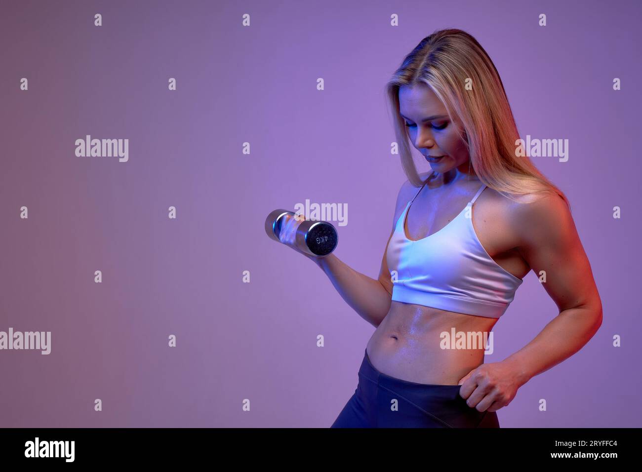 slim body of a young fit sporty woman lifting dumbbells, sweaty girl looking at her belly Stock Photo