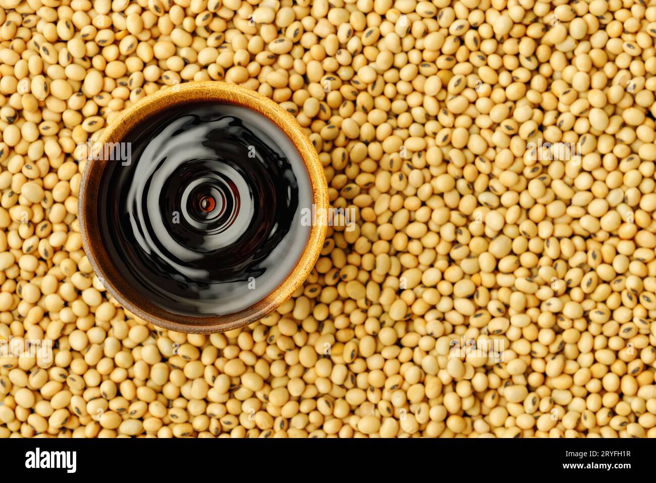 top view of soy sauce with splash in wooden bowl on dry soybeans as background Stock Photo