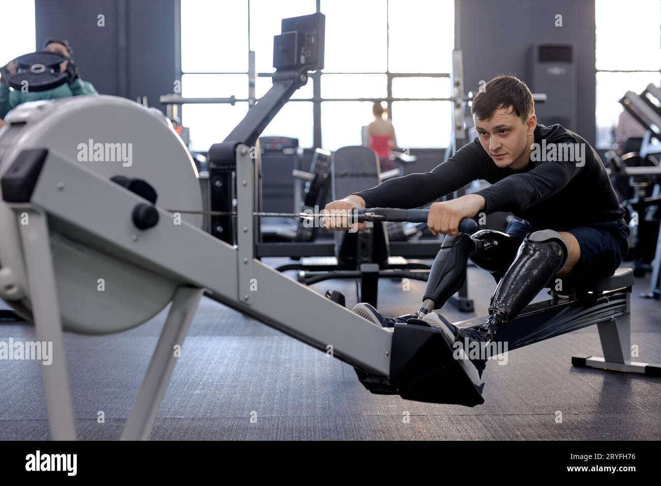 sportsman focuses on working out with stationary cardiovascular exercise machine, full length side view shot Stock Photo