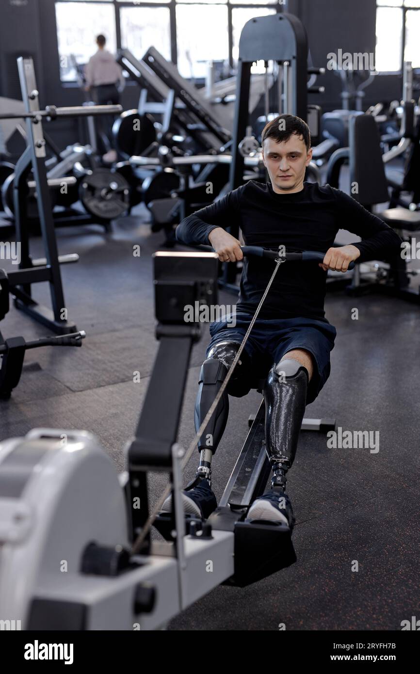 tired sweaty man training with rowing machine at gym, full length shot. motivation, endurance, willpower Stock Photo