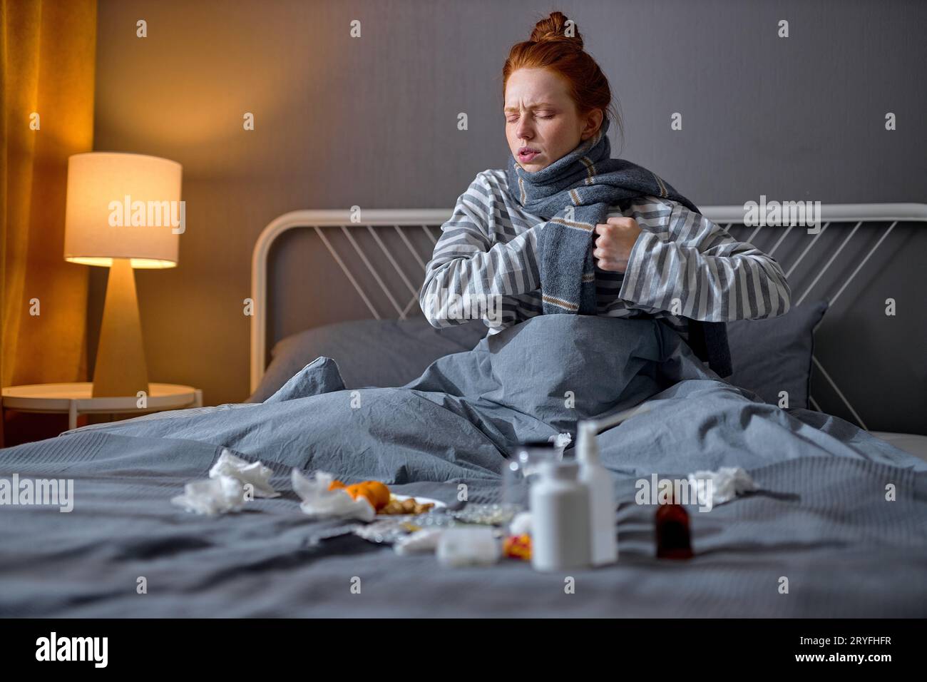 sad ginger girl sitting on bed tablets to reduce symptoms, chronic disease treatments concept, girl has problems with heart, touching it, stroke heart Stock Photo