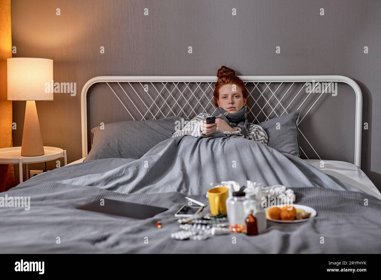 sick pale ginger woman lying in bed and with television remote control, turning on, switching off TV, television close up portrait Stock Photo