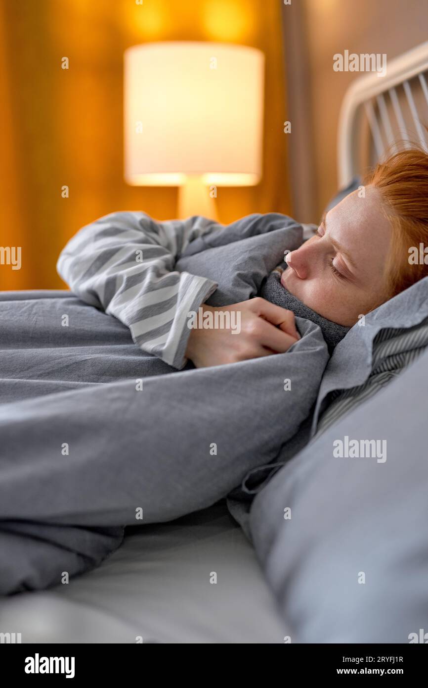 Young redhead ginger woman covered with warm blue blanket sleeping in bed at home, close up portrait side view free spare time lifestyle resting time Stock Photo