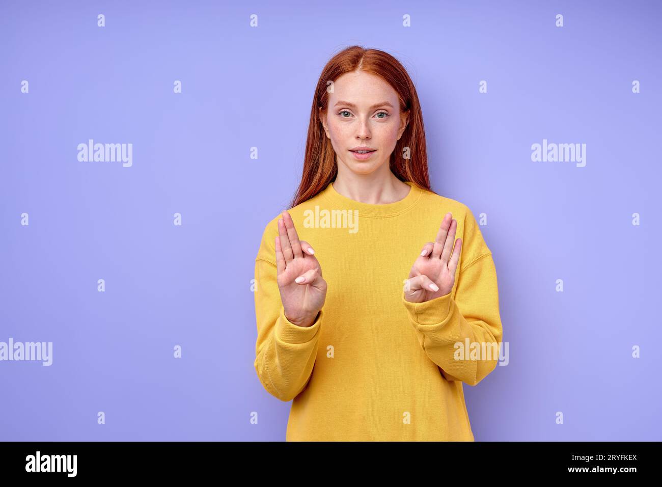 Young redhead deaf mute woman using sign language, explaining on blue background, close up portrait Stock Photo
