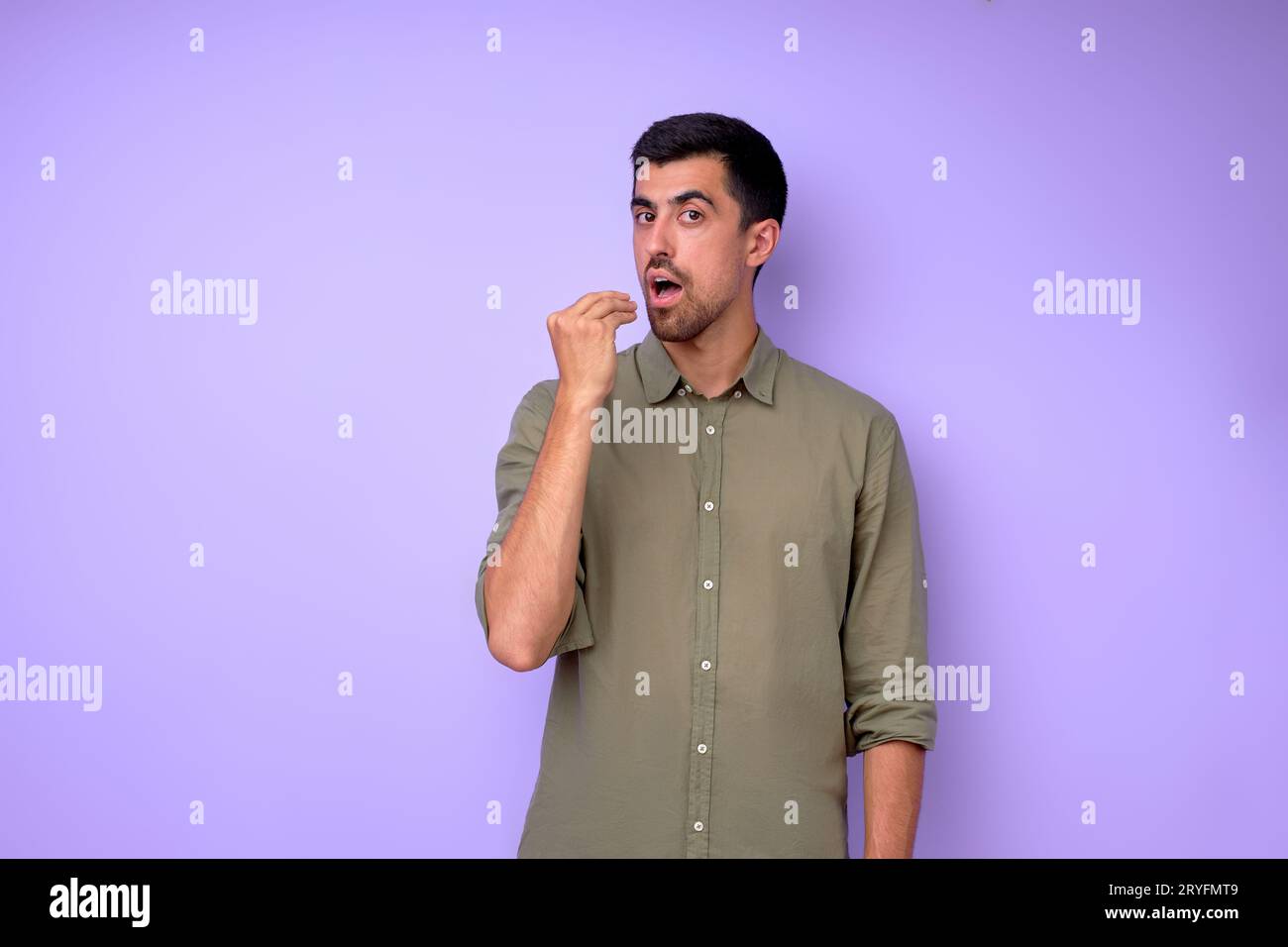 young hungry deaf man in stylish green shirt showing food gesture. guy wants to eat close up portrait isolated blue background Stock Photo