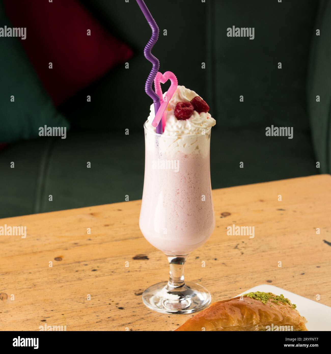 Healthy strawberry smoothie in a mug with drinking tubules next to baklava on a wooden table Stock Photo