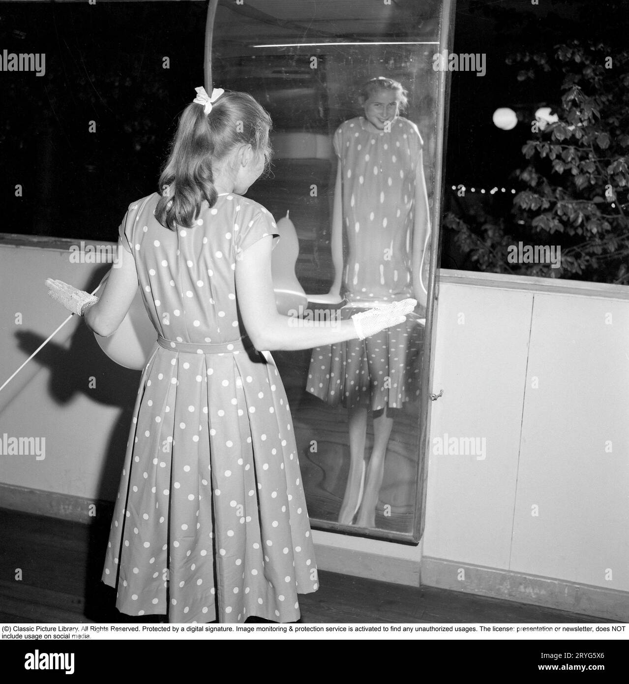 Gröna Lund amusement park in the 1950s. A teenage girl walks around the Laughing Room. A house of mirrors that you can walk around and reflect in. Depending on the type of mirror you look in, you can either be tall or short, fat or thin. The explanation is that the mirrors are either concave or convex or a combination of the two. 31 May 1958. Conard ref 3760 Stock Photo